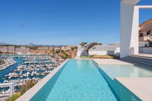 A modern infinity pool on a white terrace overlooking a busy marina and the sea under a clear blue sky.