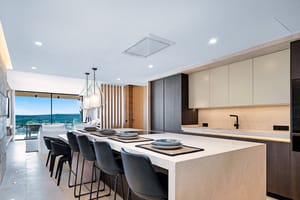 Modern kitchen with large white stone island, dark bar stools, and sliding glass doors opening to a mountain terrace.