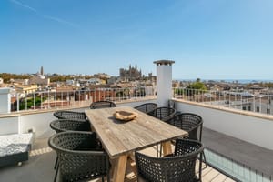 Rooftop terrace with wooden dining table and black chairs overlooking Palma Cathedral and the Mediterranean sea.