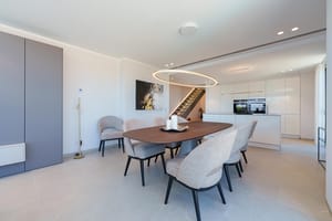 Comedor con mesa ovalada de madera y seis sillas, junto a una cocina blanca minimalista con iluminación empotrada.