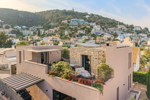 An elevated view of a contemporary villa with stone facade and rooftop terrace overlooking a hillside residential area.