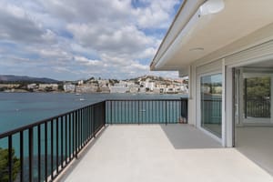 A spacious grey-tiled terrace with black metal railings faces a bay filled with boats under a cloudy sky.