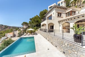 Exterior view of a cream stucco villa featuring arched terraces, wrought iron railings, stone walls, and a pool.