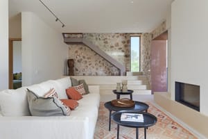 Interior view of a living room featuring a cream sofa, stone accent wall, inset fireplace, and floating staircase steps.