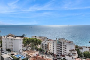 Wide-angle view looking over the Cala Mayor coastline towards the open sea with white buildings and blue water.