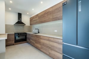 A modern kitchen in a townhouse featuring wood grain cabinets, dark appliances, stone countertops, and recessed ceiling lights.