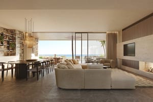 Wide-angle shot of a bright, open-plan living and dining room with floor-to-ceiling glass walls leading to an outdoor terrace, limestone fireplace, and Mediterranean sea views.