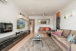 Living room featuring a brown sofa, glass coffee table, wall-mounted electric fireplace, and dark glossy media console.