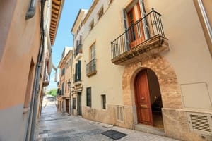 Exterior view of a multi-story townhouse in a narrow cobblestone street, featuring a stone arched entrance and iron balcony.