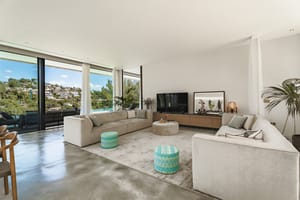 Modern living room with polished concrete floors, modular sofas, and full-height glass doors overlooking the hills.