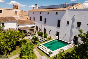 Aerial view of a white Mediterranean townhouse with a rectangular swimming pool, garden, and terracotta-tiled roof.