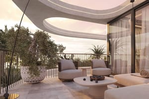 A modern curved terrace overlooking the sea at sunset, featuring stone flooring, outdoor seating, and a large potted plant.