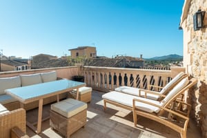 Outdoor seating and sun loungers on a rooftop terrace overlooking village rooftops and hills