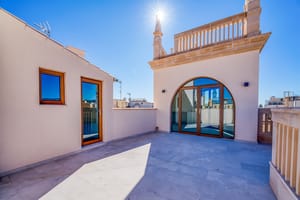 A sunny rooftop terrace with light-colored stone flooring, an arched glass door, and traditional architectural detailing.