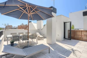 Rooftop terrace in El Molinar featuring a dining set under a grey parasol, sun loungers, and white stone flooring.