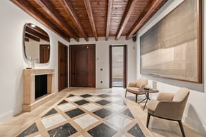 Grand entrance hall featuring dark wood ceiling beams, a checkered marble floor, and a stone fireplace with an organic mirror.