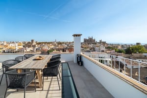 Expansive rooftop terrace with a wooden dining set overlooking the Palma city skyline and Cathedral under a clear blue sky.
