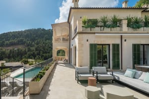 Exterior facade of a cream stone villa with a long swimming pool and shaded outdoor seating area overlooking hills.