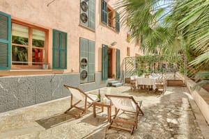 A private outdoor terrace in the Old Town featuring gravel flooring, white folding lounge chairs, a dining set, and pink stucco walls with green shutters.