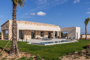 Exterior view of a single-story stone finca in Santanyí with a swimming pool, lawn, and pergola-covered terrace.