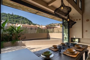Dining room with large sliding doors opening to an outdoor terrace with a pool, overlooking a hillside.