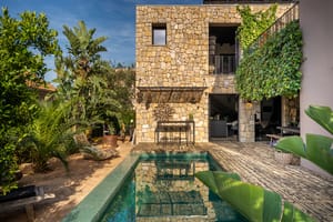 Exterior view of a stone-clad villa in Genova featuring a rectangular swimming pool, lush greenery, and climbing vines.