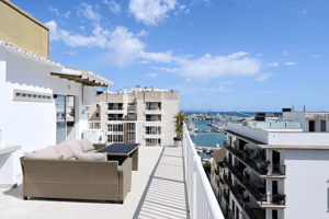 A sunny rooftop terrace overlooking the Santa Catalina marina with woven lounge furniture and a white railing.