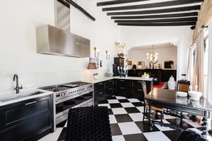 Kitchen features black and white checkered tile floors, black cabinets, a stainless steel range, and exposed dark wood beams.