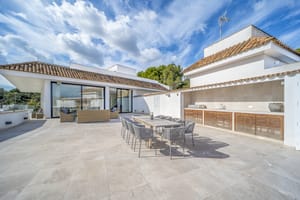 A spacious terrace in Illetas featuring a dining set, an outdoor kitchen with wooden cabinetry, and large sliding glass doors.