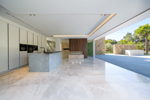 Modern open-plan kitchen with a stone island, floor-to-ceiling sliding glass doors, and polished marble flooring.