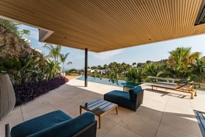 A covered terrace with a wood-slatted ceiling, limestone flooring, and blue outdoor lounge furniture overlooking a swimming pool.
