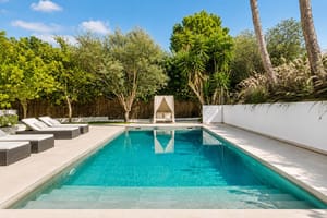 Rectangular swimming pool with tiled interior, sun loungers and canopy daybed surrounded by mature Mediterranean planting