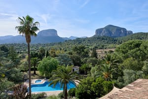 Wide shot of a Mallorca finca estate featuring a swimming pool, palm trees, and the Tramuntana mountain range in the distance.