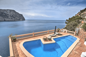 An L-shaped swimming pool with blue water sits on a terracotta-tiled terrace overlooking the sea at Cala Llamp.