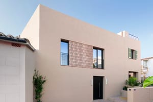Minimalist sand-colored townhouse facade with a perforated terracotta screen, dark entrance door, and integrated planters.