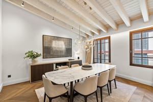 Contemporary dining room featuring a white marble table, upholstered chairs, and exposed white-washed ceiling beams.
