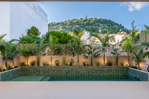 A rectangular pool with green chevron tiling and tropical plants, set against a backdrop of the Na Burguesa hills.