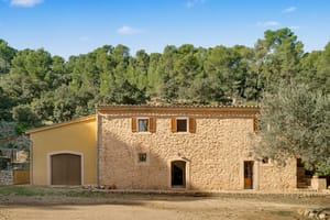 Two-storey stone finca façade with wooden shutters and dry-stone walls