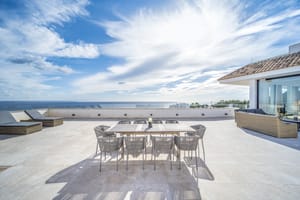 A wide sun-drenched stone terrace featuring an outdoor dining set and lounge chairs overlooking the Mediterranean sea.