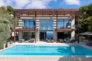 Exterior of a contemporary villa featuring an infinity pool, natural stone facade, floor-to-ceiling glass, and timber pergola.