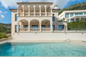 Two-story Mediterranean villa featuring stone arches and balustrade balconies overlooking a rectangular swimming pool.