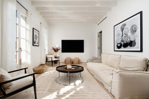Living room with black cane armchairs, a cream linen sofa, black round coffee tables and framed black and white photography.