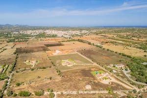 High-altitude aerial view of rural Mallorcan landscape near Santanyí, featuring sparse vegetation and distant town buildings.