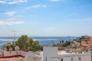 Elevated view overlooking the San Agustin coastline and Mediterranean sea under a clear blue sky with urban rooftops below.