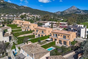 Aerial drone view showing a row of terraced townhouses with ochre facades, landscaped gardens, and a pool in Es Capdella.