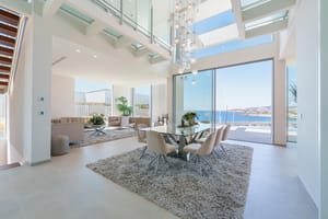 Double-height living and dining space with floor-to-ceiling sliding glass doors opening to a coastal view.