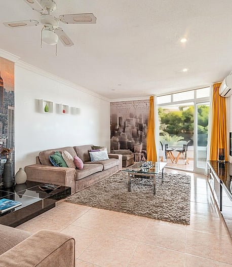 Wide-angle view of a living room featuring a plush sofa, high-gloss TV unit, and floor-to-ceiling glass doors opening to a terrace.