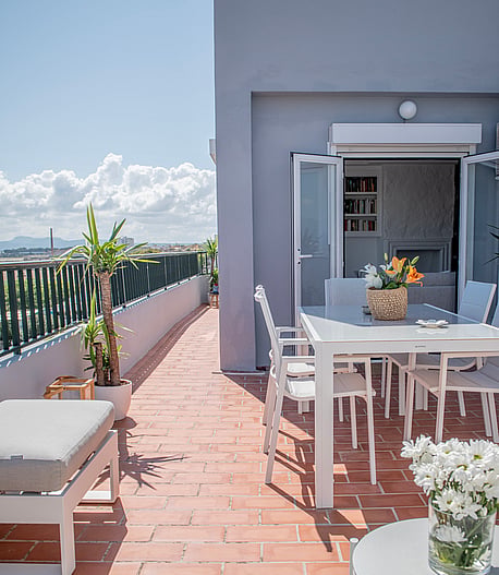 A sunlit rooftop terrace in El Molinar with a white dining set, terracotta tiles, and mountain views in the background.