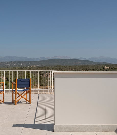 Elevated stone terrace with two wooden chairs facing a mountain landscape under a clear blue sky.