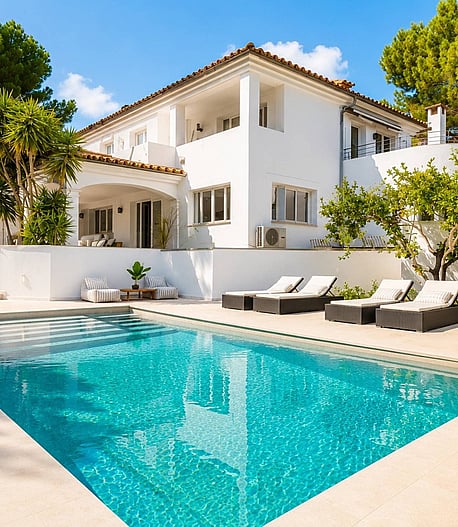 Rear view of a white two-storey villa in Santa Ponsa with rectangular pool, sun loungers and terracotta tile roof